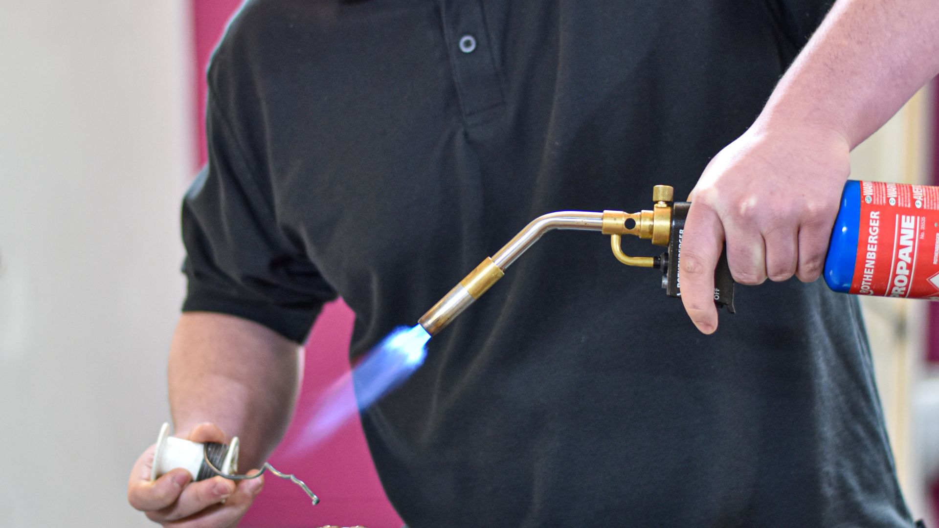 A man holding a blowtorch working on some copper pipes.