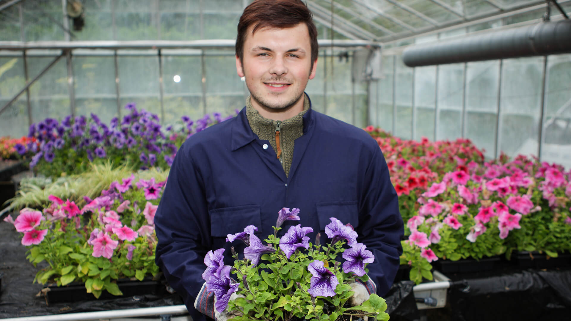 Smiling male student holding flowers in a greenhouse